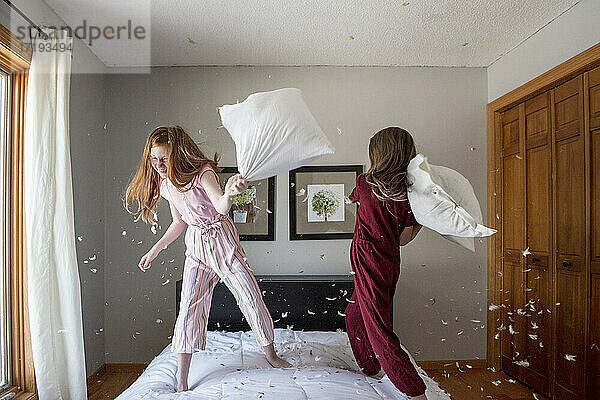 Zwei glückliche junge Mädchen  die auf dem Bett eine Federkissenschlacht machen.