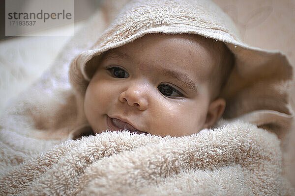 Ein in ein Handtuch eingerolltes Baby  das sich in der Badewanne umschaut und lächelt