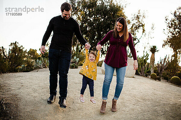 Mama und Papa heben lächelnde Tochter im Kaktusgarten im Balboa Park hoch