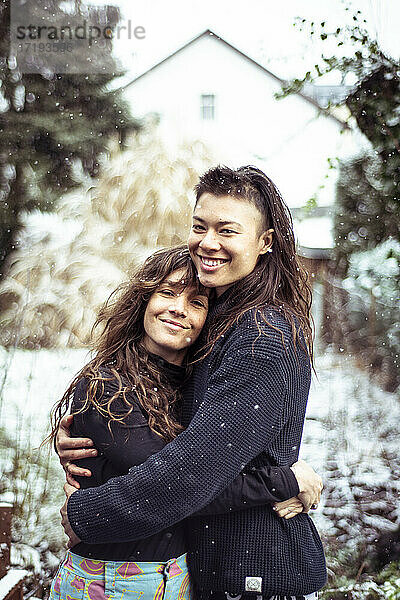 gemischtrassiges queeres frauenpaar umarmt und lächelt im schnee in europa winter