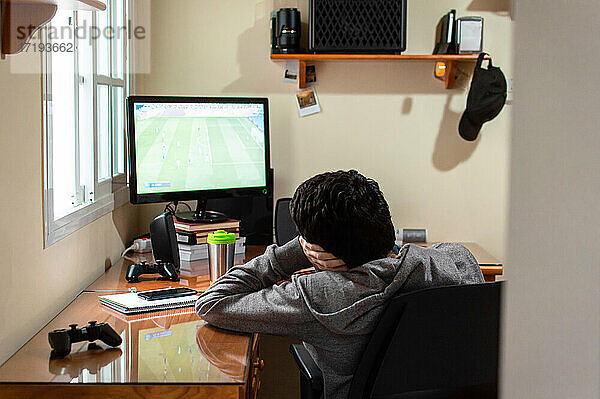 Ein gelangweilter Mann sitzt in seinem Zimmer und sieht sich ein Fußballspiel im Fernsehen an.