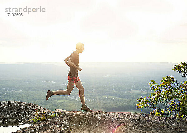 Erwachsener männlicher Trailrunner auf einem Bergkamm bei Sonnenuntergang