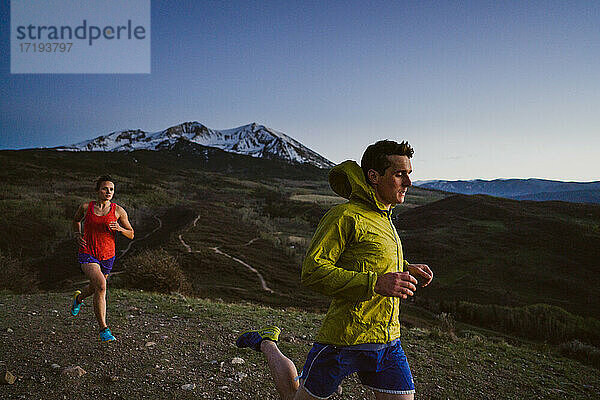 Junger Mann und Frau Trailrunning in der Dämmerung mit Blick auf die Berge