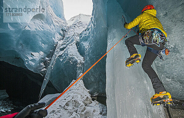 Mann klettert auf Eiszapfen in einer Gletscherhöhle in Island