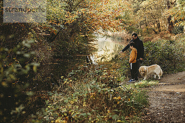 Vater zeigt auf Kanal mit Sohn und Hund im Herbst