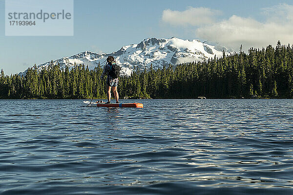 Rückansicht einer nicht erkennbaren Frau  die auf dem kräuselnden Wasser eines Sees in der Nähe eines verschneiten Berghangs paddelt