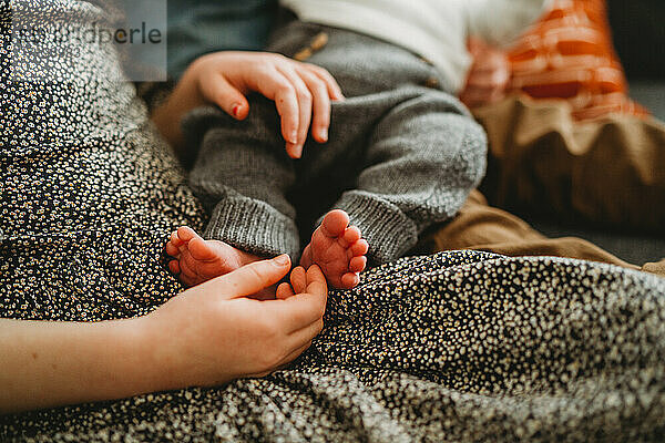 Nahaufnahme eines älteren Kindes  das die Füße eines Neugeborenen zu Hause hält