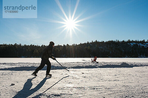 Ein Jugendlicher spielt Hockey auf einer Eisbahn auf einem zugefrorenen See in Kanada.