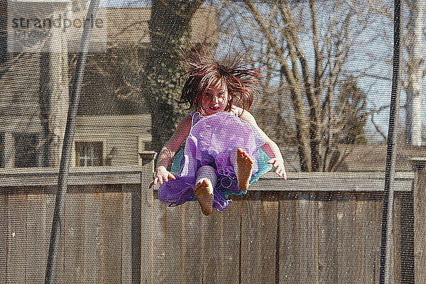 Kleines Mädchen mit fehlenden Zähnen und buntem Kleid springt auf Trampolin