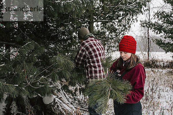 Junge und Mädchen in Winterkleidung beim Schneiden von Tannenzweigen für Weihnachten