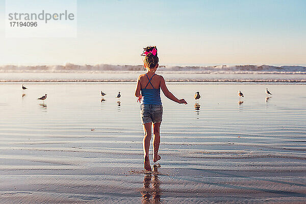 Ein Mädchen im Schulalter läuft am Strand auf das Wasser und die Vögel zu.