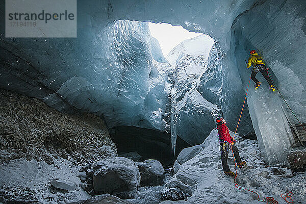 Männer klettern auf Eiszapfen in einer Gletscherhöhle in Island