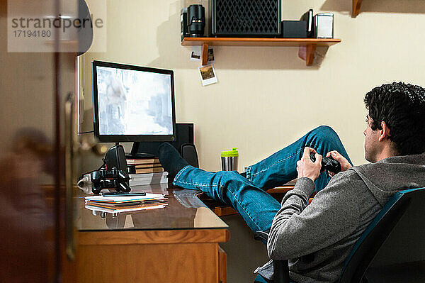 Junger Mann in Sweatshirt und Jeans  der in seinem Schlafzimmer Videospiele spielt.