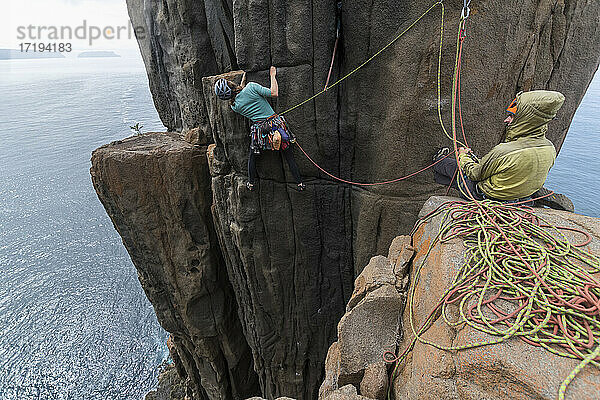 Ein abenteuerlustiges Paar klettert auf den ausgesetzten Felspfeilern von Cape Raoul  wobei die Frau zwei Seile als Schutz benutzt  während sie versucht  einen Weg nach oben zu finden  und der Mann sie in Tasmanien  Australien  sichert.