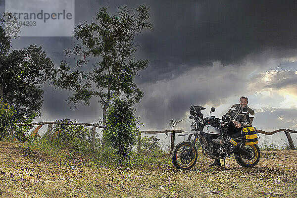 Ein Mann posiert auf seinem Geländemotorrad vom Typ Scrambler in Thailand
