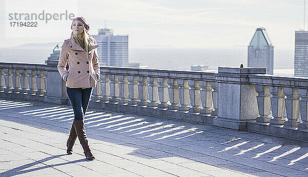 Blonde Frau mit rosa Mantel und Stadt im Hintergrund