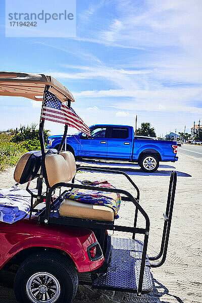 Golfwagen geparkt am Strand mit amerikanischer Flagge und Pickup-Truck sein