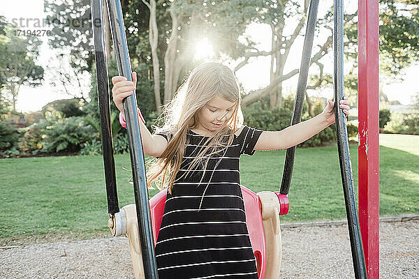 Junges lächelndes Mädchen  das auf einer Schaukel auf einem öffentlichen Spielplatz steht