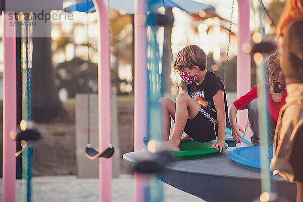 Junge mit Maske spielt allein auf einem Spielplatz