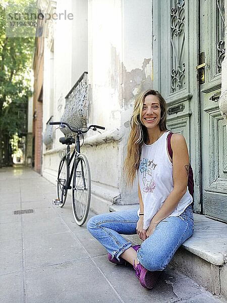 Glückliche Frau  die vor einem Gebäude auf einem Fahrrad sitzt