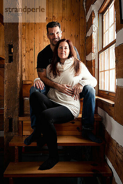 Attraktives Paar sitzt zusammen auf einer Treppe in einem rustikalen Blockhaus.
