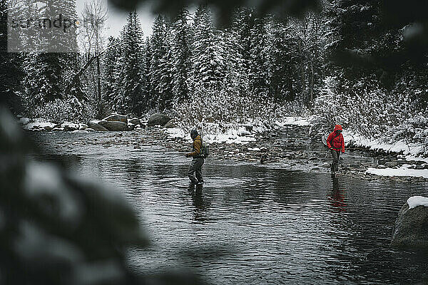 Mann und Frau spazieren im Fluss beim Fliegenfischen im Winter im Urlaub