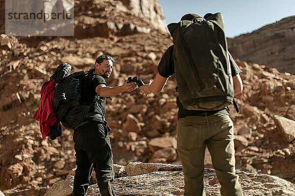 Mann gibt einem Freund ein Fernglas beim Wandern auf einem Berg im Canyonlands National Park