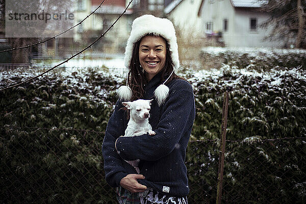 Asiatische Frau lächelt in die Kamera weißen weißen flauschigen Hut und weißen Hund Hund