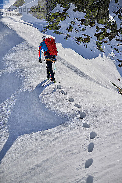 Ein Mann besteigt an einem sonnigen Tag einen verschneiten Berg in Devero  Italien.