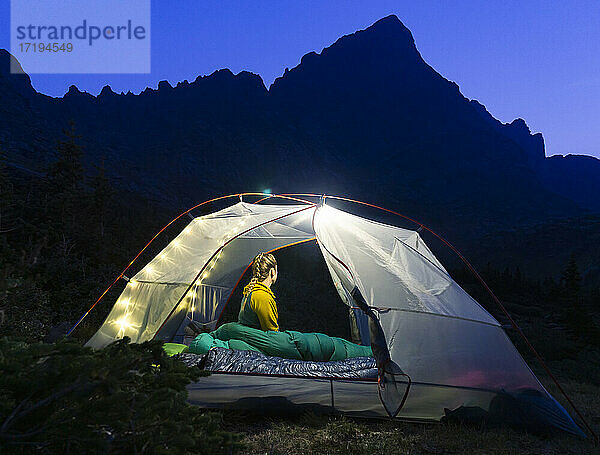 Frau sitzt in beleuchtetem Zelt auf einem Berg bei Nacht