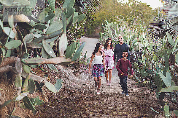 Eine vierköpfige gemischtrassige Familie geht auf einem Kakteenpfad spazieren.