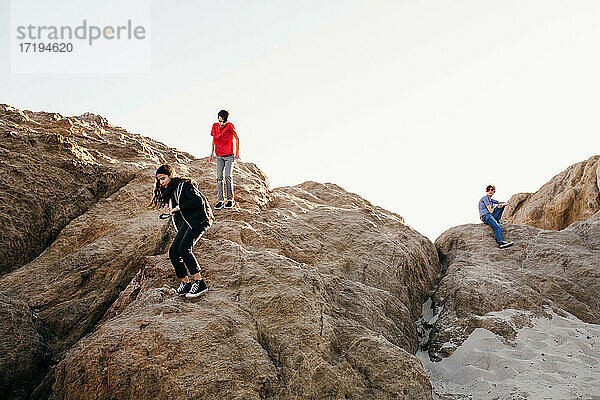 Geschwister am Strand klettern auf große Felsen