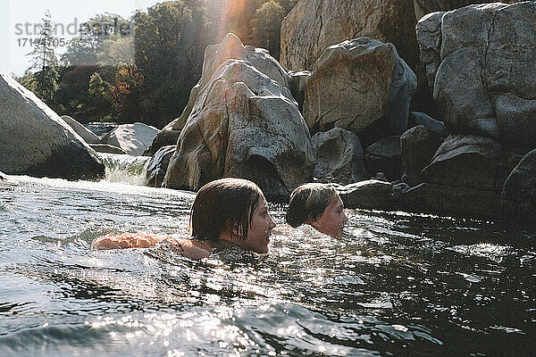 Freunde schwimmen gemeinsam neben einem Wasserfall im Yuba River