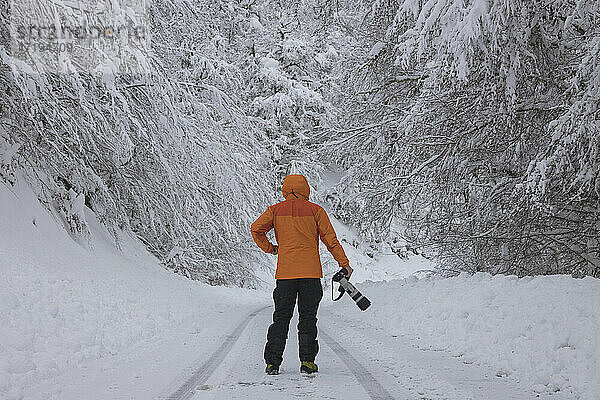 Fotograf wartet über verschneiter Straße im Wald
