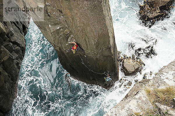 Ein Kletterer klettert auf dem Totempfahl aus dem Meer in Cape Hauy  Tasman National Park  Tasmanien  Australien.