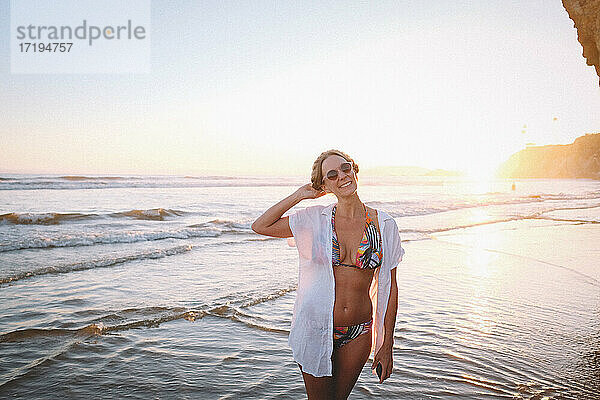 Frau im tropischen Bikini am Strand bei Sonnenuntergang