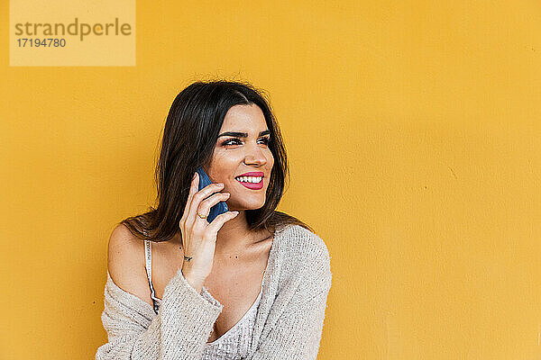 Porträt eines spanischen brünetten Mädchens  das auf einer Wand mit gelbem Hintergrund mit einem Mobiltelefon spricht.