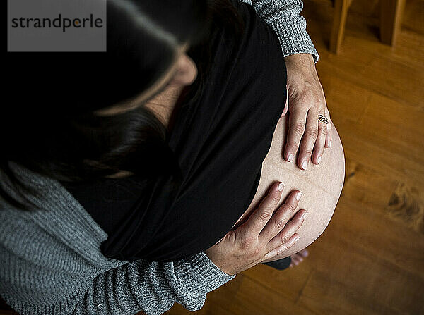Blick von oben auf eine schwangere Frau  die ihren Bauch zu Hause mit den Händen berührt