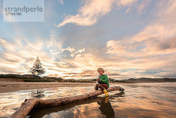 Lockenköpfiges Kind spielt mit Sand bei Sonnenuntergang am neuseeländischen Strand