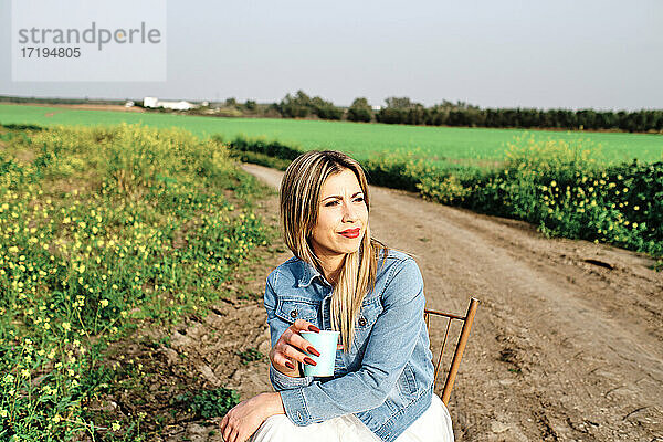 junge Frau  die auf einem Stuhl sitzend einen Kaffee auf dem Land genießt