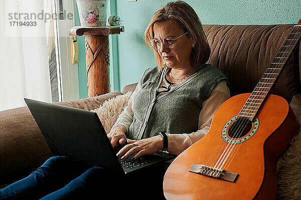 Frau mittleren Alters lernt zu Hause mit einem Laptop Gitarre spielen