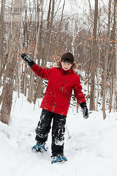 Junger Junge beim Schneeschuhwandern im Wald an einem verschneiten Wintertag.