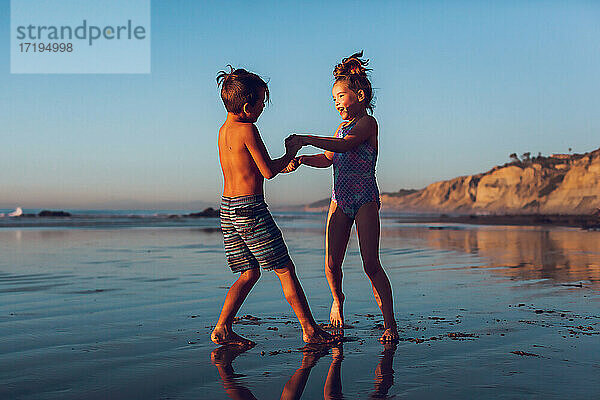 Junge und Mädchen spielen am Strand zur goldenen Stunde Ring um die Rose.