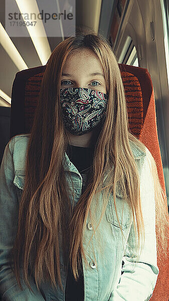 glückliches Mädchen in einem Transportmittel  das eine Maske trägt und in die Kamera schaut