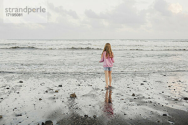 Junges Mädchen  das in der Abenddämmerung am Strand am Wasser steht