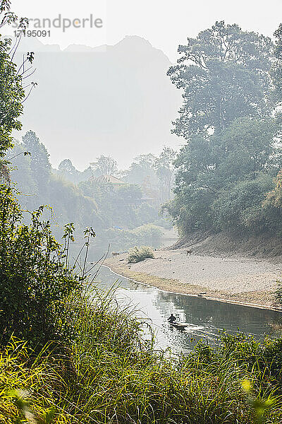 Mann rudert Boot auf stillem Fluss in Laos