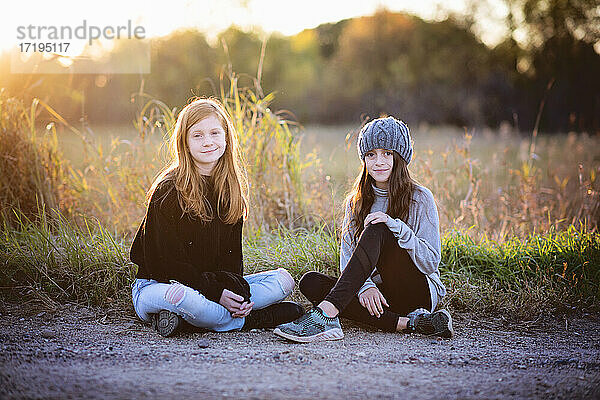 Zwei hübsche junge Mädchen sitzen im Herbst im Freien  im Gegenlicht.