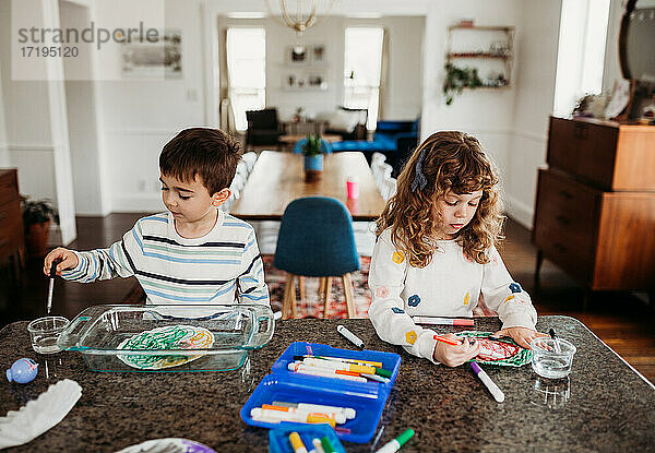 Kleiner Bruder und kleine Schwester malen mit Markern am Küchentisch