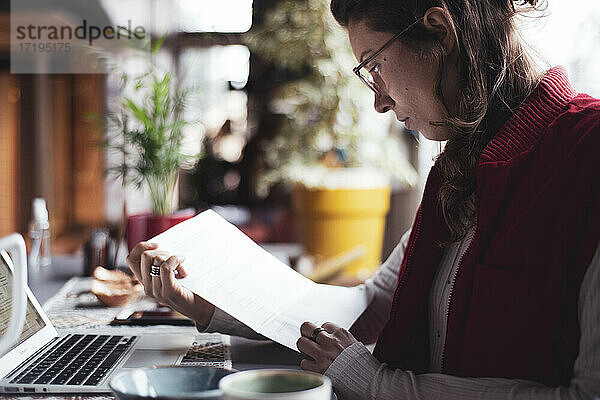 Geschäftsfrau liest Papierkram mit Laptop im Büro zu Hause  während sie sich ausruht