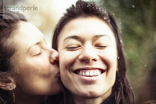 Mädchen küsst lächelndes Mädchen auf die Wange  während im Winter Schnee in die Haare fällt